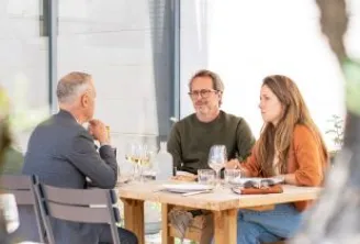 Three people seated at a table in a restaurant at Chais de la Fleur in Bordeaux, conversing over glasses and plates