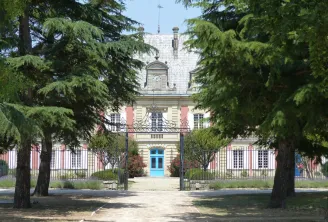 Facade of Château Saint Ahon in Bordeaux, a pink and white building with a blue door, framed by ancient trees and a paved pathway.