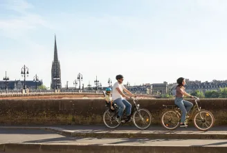 Three cyclists riding bikes along Bordeaux waterfront with Saint-Michel Basilica in the background