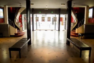 Entrance hall of Bordeaux's Trianon Theatre featuring glass doors, black columns, benches and theatrical posters, Art Deco style