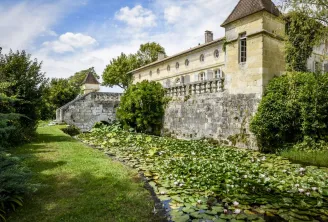 Château Beauregard in Bordeaux featuring stone facades, pointed tower, and water lily pond in the foreground, surrounded by lush greenery