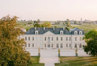Aerial view of Château Soutard, an elegant white manor house with blue slate roofs and a central paved pathway, surrounded by manicured gardens and Bordeaux vineyard landscapes