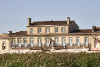 Classic stone facade of a Bordeaux mansion with wrought iron balcony overlooking vineyards in Bordeaux.