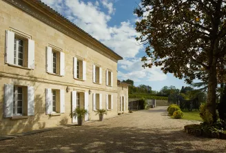 Elegant facade of Château Bernateau in Bordeaux, stone building with white shutters, gravel driveway and vineyard landscape in the background