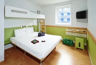 Modern hotel room at Ibis budget Bordeaux with white double bed, bunk bed, lime green and white walls, wall-mounted TV, window, and built-in storage.
