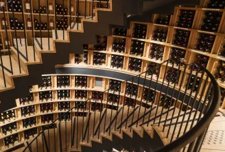 Spiral wine cellar with wooden shelves holding hundreds of wine bottles, black metal staircase winding through the space, in Bordeaux.