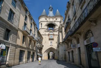 The Grosse Cloche of Bordeaux, a 13th-century medieval tower with three conical turrets, framed by historic buildings on a paved street in the old town.