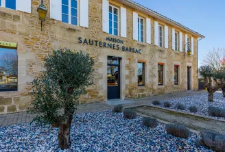 Stone facade of the Sauternes Barsac House in Bordeaux, featuring blue-framed windows, entrance door, and blue gravel garden with olive trees