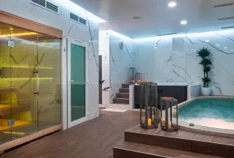 Luxurious spa facility featuring a yellow-lit sauna, turquoise pool with artificial beach, white marble walls, modern LED lighting and greenery at Spa Nuxe in Bordeaux