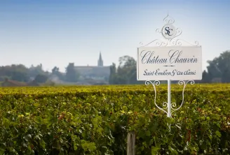 Ornamental sign for Château Chauvin, a Saint-Émilion Grand Cru wine estate, displayed in vineyard rows with the village church visible in the background