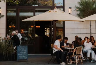 Outdoor terrace of French House restaurant in Bordeaux with customers seated under beige umbrellas, modern storefront with French signage