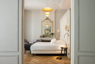 Elegant bedroom at Hôtel Villas Foch in Bordeaux featuring a white bed, herringbone parquet floor, golden mirror, gold lighting fixtures and luxury furnishings
