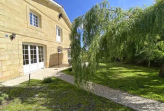 Stone house facade with paved terrace, white French doors and weeping willow in a sunny green garden