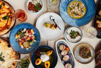 Restaurant table featuring gourmet dishes including pizzas, curries, tartares and colorful accompaniments, with rosé wine glasses and water, in a modern fine dining setting.