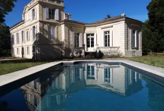 Mayne La Merci Castle in Bordeaux featuring a white stone neoclassical mansion with a square tower, reflected in a modern swimming pool in the foreground.