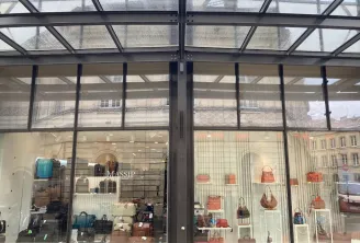 Storefront of Massip Maroquinerie in Bordeaux displaying leather handbags and accessories in various colors through glass windows beneath an architectural glass canopy.