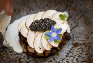 Gourmet plate from Passage Secret restaurant in Bordeaux: chocolate éclair topped with caviar, seared foie gras slices, and edible blue flower on grey sauce.