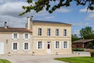 Cap Léon Veyrin estate near Bordeaux, a refined stone house with pale yellow facade, regular windows, gravel driveway, green lawn and oak branch in the foreground