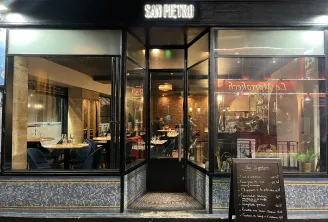 Storefront of San Pietro restaurant in Bordeaux, featuring illuminated windows displaying the interior with dining tables and guests, neon sign, and menu board at the entrance.
