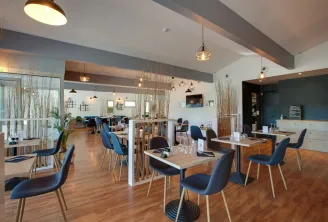 Modern interior of Apolonia restaurant in Bordeaux featuring wooden tables, blue chairs, pendant lighting, and natural fiber room dividers.