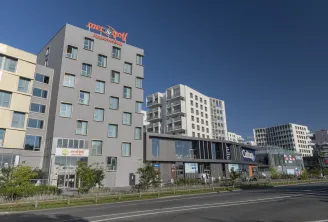 View of the Mer & Golf City Bordeaux Lac apart-hotel featuring modern multi-story buildings in grey and white tones, located in the Lake district of Bordeaux, under a clear sky.