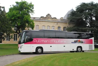 White and pink Pullman d'Aquitaine coach bus parked in front of a historic château in Bordeaux, with lawn and trees in the background