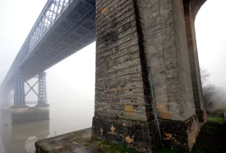 Misty view beneath Bordeaux's stone bridge showing massive stone pillars and the metal structure of the Eiffel bridge in the background, with green algae on the foundations.