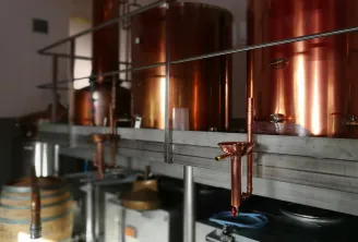 Interior of Moon Harbour distillery in Bordeaux featuring glowing copper stills, copper piping, a metal railing, and a wooden barrel in the foreground.