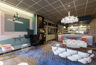 Modern lobby of Ibis Styles Bordeaux Meriadeck hotel featuring a bar counter, contemporary seating area with white and orange furniture, geometric ceiling design, and stylish interior décor