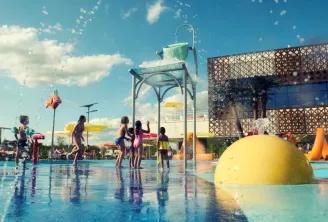 Children playing in a water park with water sprays, yellow dome and play structures under a sunny blue sky