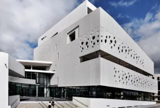 Modern white façade of the Bordeaux Maritime Museum featuring circular perforations, access stairs, and blue sky backdrop