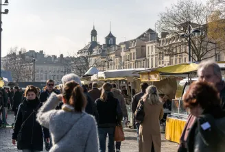 Bustling market at Quai des Chartrons in Bordeaux with visitors browsing yellow market stalls, Haussmann-style buildings and churches in the background.