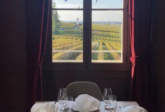 Elegant dining room table set with white napkins and glasses overlooking Bordeaux vineyards with hot air balloons floating in the blue sky