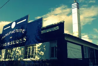 Bordeaux's La Manufacture industrial building featuring blue 'Shoe Manufacturing' sign and white chimney against a clear blue sky