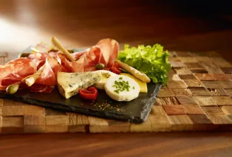 A charcuterie and cheese board on a black slate with Parma ham, blue cheese, fresh mozzarella, toasted breadsticks, pickles, lettuce and fresh herbs on a wooden board in Bordeaux.
