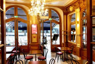 Elegant interior of QuatrèS Café in Bordeaux featuring golden wood paneling, crystal chandelier, wooden glass doors, and classic furniture with outdoor terrace visible.