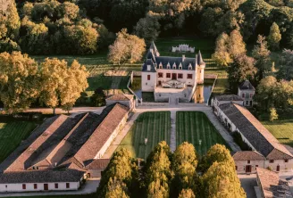 Aerial view of Château Olivier in Bordeaux, displaying the castle with its towers, surrounding vineyards, and wine production buildings, surrounded by autumn forest.