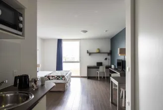 Modern studio apartment at Ténéo Aparthotel in Bordeaux-Maritime featuring a bed, equipped kitchenette, work area, large window with balcony and contemporary decor