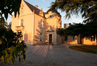 Château La Haye in Bordeaux, an elegant 18th-century mansion with golden-yellow facades illuminated by sunset light, surrounded by greenery and accessed by a paved courtyard