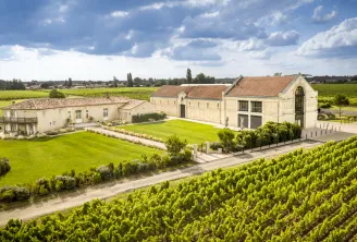 Château La Garde in Bordeaux featuring white stone buildings surrounded by lush vineyards and manicured lawns under a partly cloudy sky