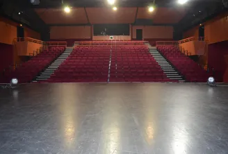 Interior of a modern cinema theater featuring red stadium-style seating, a black screen, orange walls, and a black ceiling with lighting fixtures.