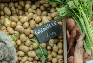 Market stall at Saint-Augustin Market in Bordeaux displaying fresh vegetables including beets, potatoes, small grenaille potatoes, and parsley with handwritten price signs.