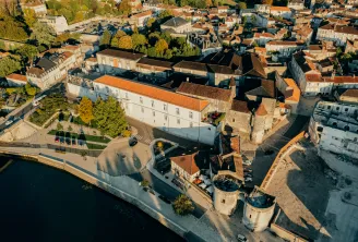 Aerial view of Cognac Castle in Bordeaux showing fortified towers along the waterfront, surrounded by historic buildings and the medieval city