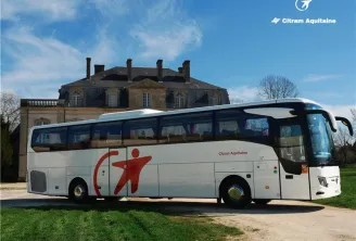 A white Citram Aquitaine bus parked in front of a historic castle in Bordeaux, displaying its distinctive red logo on the side of the vehicle.