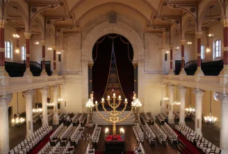 Interior of the Bordeaux Synagogue featuring a central nave, lateral galleries, ornamental columns, prayer benches, golden chandeliers and the golden ark above the altar