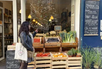 Storefront of a gourmet grocery store in Bordeaux displaying fresh produce in wooden crates, a hand-drawn map of France on the window, and daily menu on a blue chalkboard.