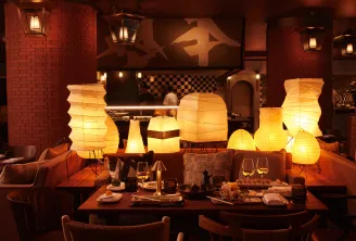 Morimoto restaurant in Bordeaux featuring an elegant dining room with red brick walls, set tables, modern chairs, and white paper lantern lights creating a warm and sophisticated atmosphere.