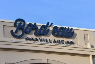 Blue sign of Bord'eau Village shopping center in Bordeaux, featuring stylized logo and geometric mountain patterns on beige facade