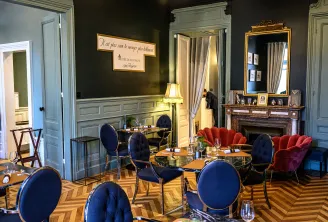 Elegant room at Cercle de Montaigne in Bordeaux featuring blue and red chairs, black tables, herringbone flooring, marble fireplace, gilded mirror, and framed French quote on dark wall.