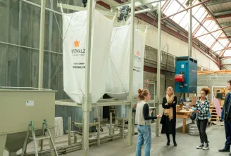 Guided tour of the Bestmalz brewery in Bordeaux with visitors observing fermentation tanks and brewing equipment in an industrial warehouse.